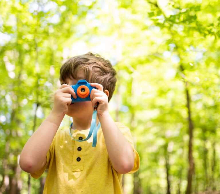 A small child in a yellow shirt taking a picture using a toy camera in Tunica Hills
