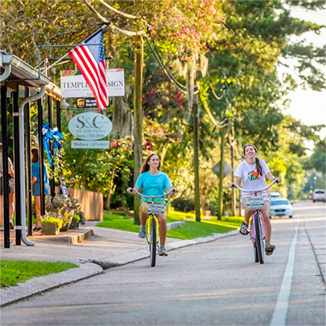 Two women on bikes cruising down the street by a shop