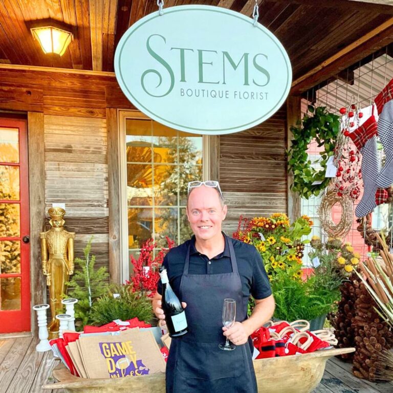A man holding a champagne bottle and glass outside of Stems Boutique Florist